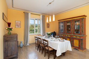 A dining room with a table set for four, a cabinet with glass doors, and a window with curtains. - A typical Italian Villa in the center of Italy.  (spoleto)