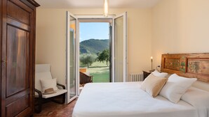 A bedroom with a large bed, a chair, and a view of a garden through an open door. - A typical Italian Villa in the center of Italy.  (spoleto)