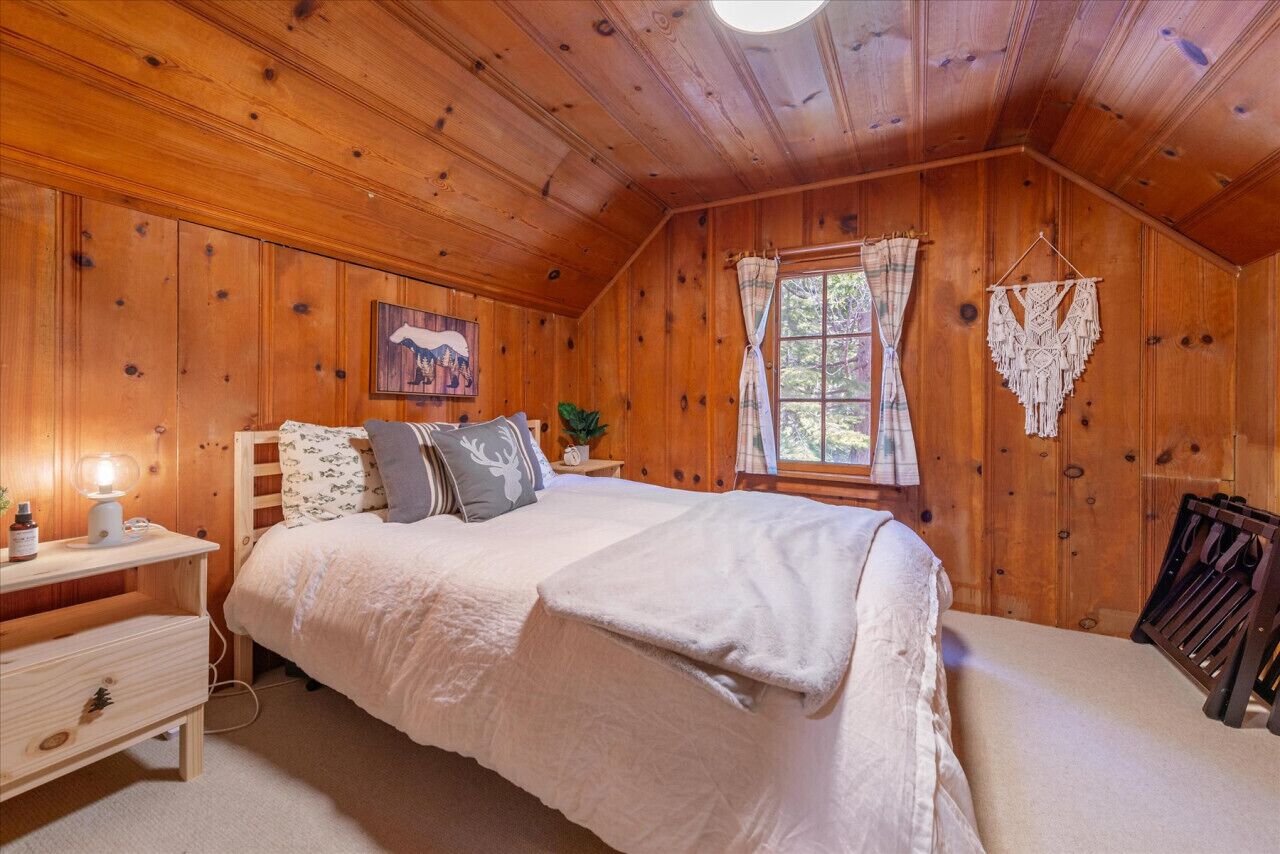 A cozy wooden cabin bedroom with a bed, nightstand, and a hanging macrame piece.