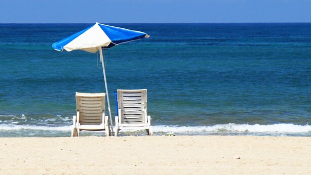 Deux chaises de plage et un parasol bleu et blanc sur une plage de sable, avec l’océan en arrière-plan.