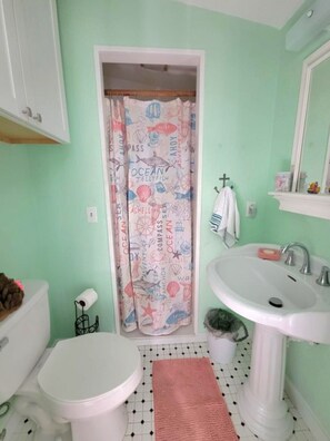 Un baño con inodoro blanco, lavamanos y cortina de ducha con motivos marinos.