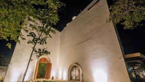 Un edificio con un'ampia entrata ad arco, un vialetto in pietra che vi conduce e un interno ben illuminato visibile attraverso l'arco.