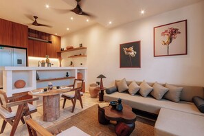 Un salon moderne avec une table à manger en bois, un canapé et des chaises. On y trouve également un coin cuisine avec des meubles en bois et un ventilateur de plafond.