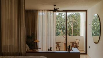 A modern bedroom with a large bed, a desk with a lamp, and a view of the outdoors through a sliding glass door.