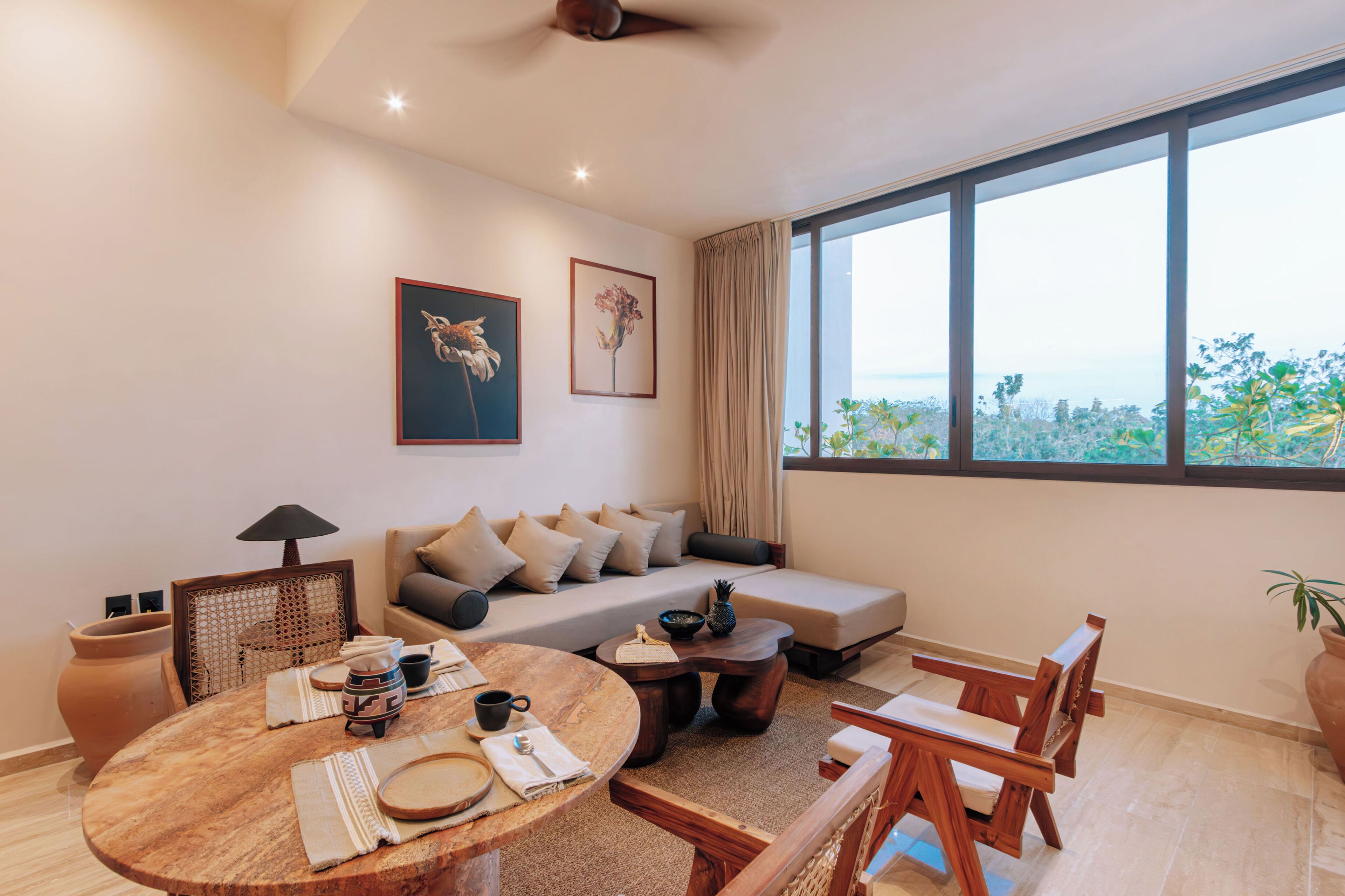 A modern living room with a sofa, a round wooden table, and a large window offering a view of the outdoors.