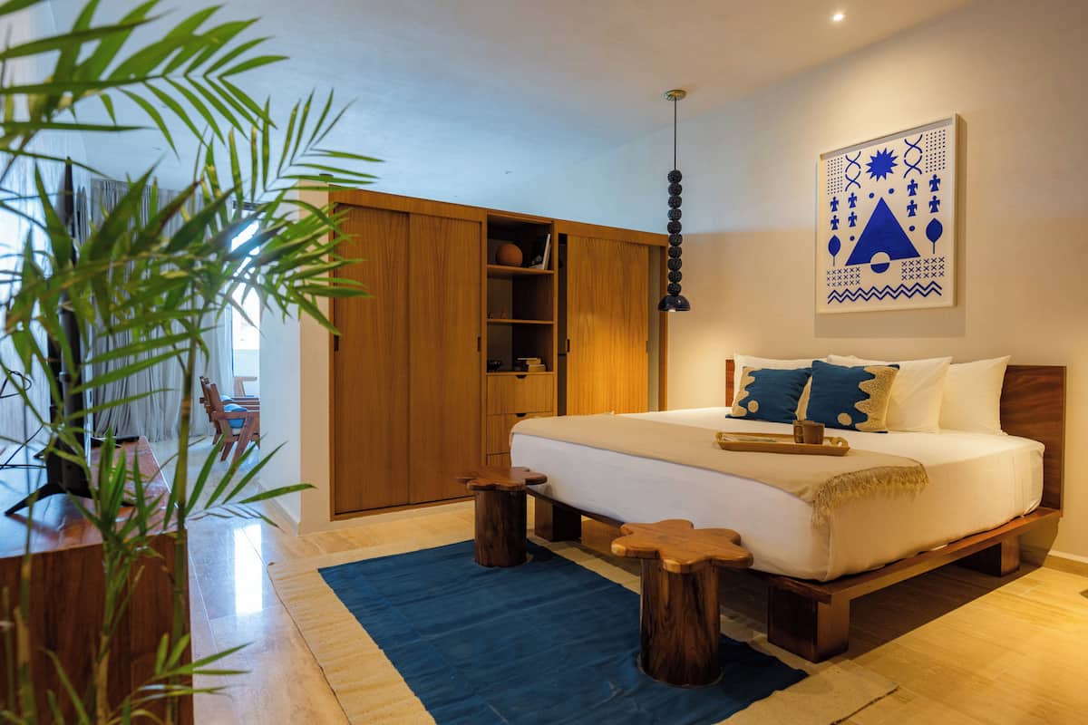 A bedroom with a bed, wooden wardrobe, bedside tables, a hanging light, and a wall art piece.