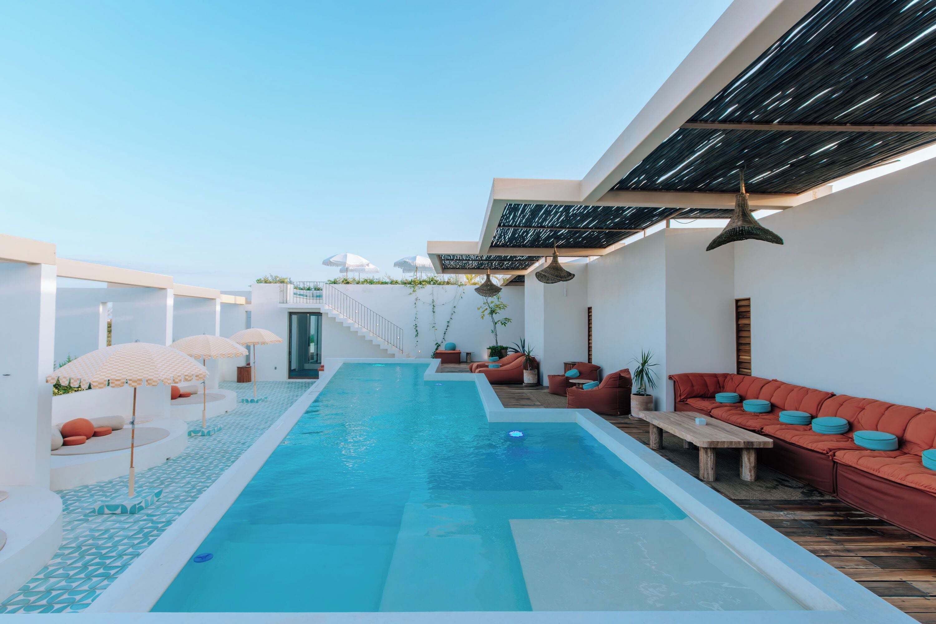 A modern outdoor pool area with a long pool, sun loungers, and umbrellas.