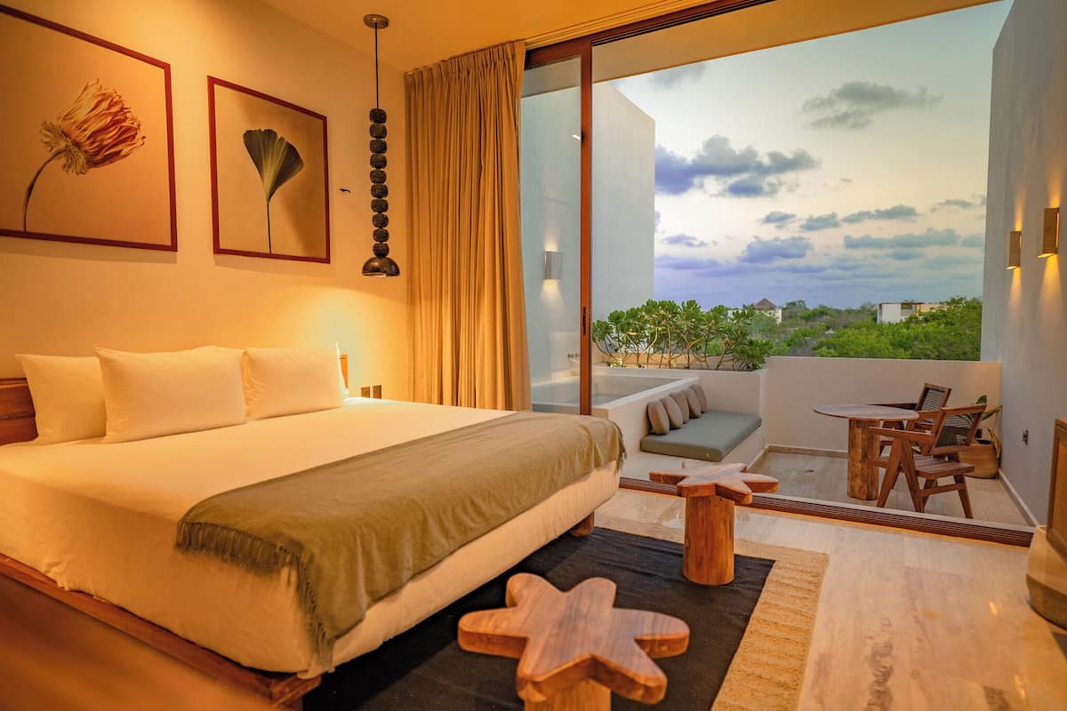 A modern hotel room with a large bed, a balcony with a view, and a dining area.