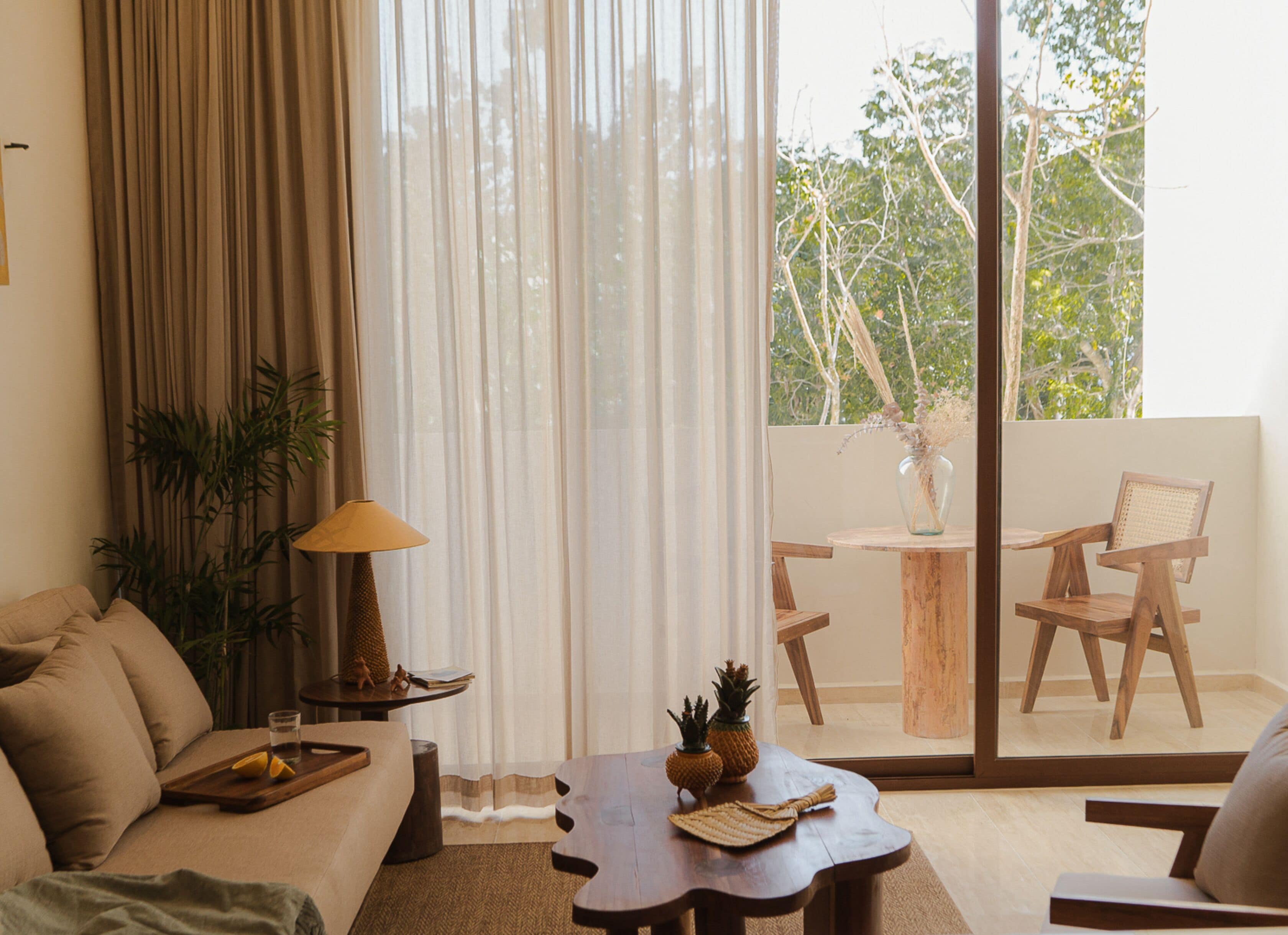 A living room with a sofa, a coffee table, a lamp, and a view of a balcony with chairs and a table.