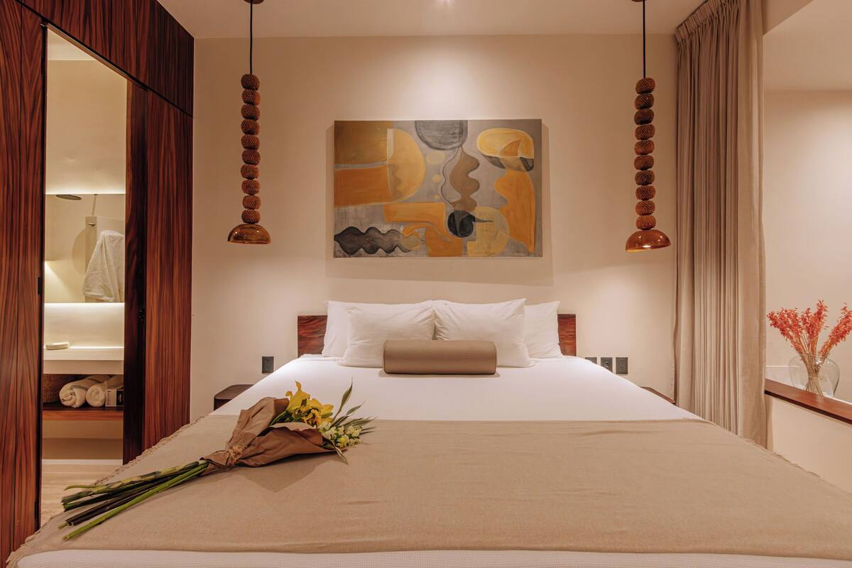 A hotel room with a bed, a painting on the wall, and a bouquet of flowers on the bed.