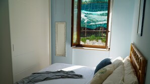 Een slaapkamer met een bed, een raam met uitzicht op groen en een houten hoofdbord.