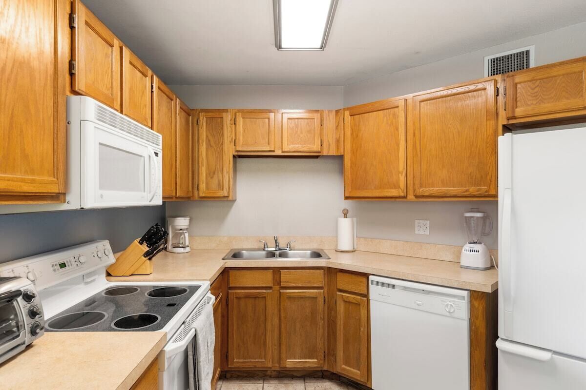 Una cocina con armarios de madera, estufa, microondas, lavavajillas y licuadora.