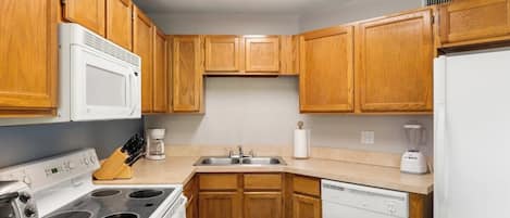 Una cocina con armarios de madera, estufa, microondas, lavavajillas y licuadora.