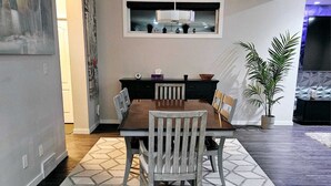 Un'area pranzo con un tavolo e sedie in legno, un tappeto a motivi geometrici, una lampada a sospensione e una pianta in vaso.