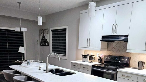 Una cucina moderna con isola centrale, sgabelli da bar, piano cottura e mobili bianchi.