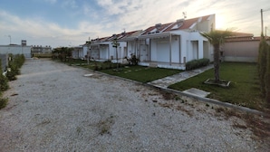A row of white buildings with red-tiled roofs, a gravel driveway, and a grassy area with a palm tree. - Danai Maisonettes Ofriniou  (Pangaio)