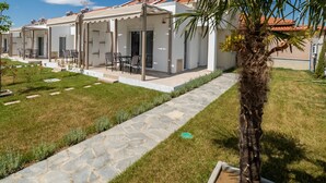 A row of white buildings with covered outdoor seating areas and a stone pathway. - Danai Maisonettes Ofriniou  (Pangaio)