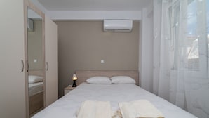 A neatly made bed with two towels, a bedside lamp, and an air conditioning unit above the headboard. - Danai Maisonettes Ofriniou  (Pangaio)