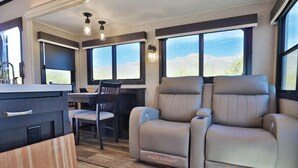 A modern RV interior with a dining area, two reclining seats, and a kitchen counter. - Sonoran Serenity (Tucson)