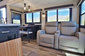 Un interior moderno de autocaravana con comedor, dos asientos reclinables y una encimera de cocina.