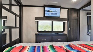 A hotel room with a bed, a television mounted above a window, and a door. - Sonoran Serenity (Tucson)