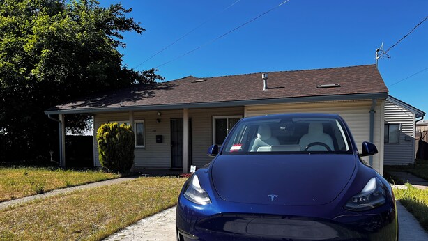 A blue Tesla parked in front of a single-story house with a front porch and a small front yard. - Adorable Home for Family. (Stockton)