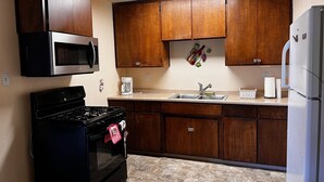 A kitchen with wooden cabinets, a microwave, a stove, a sink, and a refrigerator. - Adorable Home for Family. (Stockton)