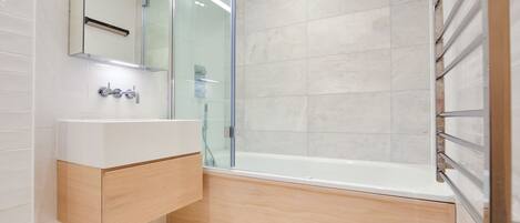 Un baño moderno con cabina de ducha de vidrio, un lavabo blanco y un mueble de tocador de madera.