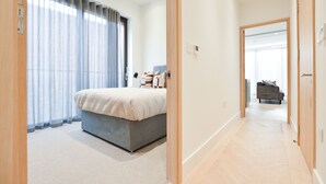 A modern bedroom with a large bed, a bedside table, and a window with sheer curtains. - Haverstock Hill Serviced Apartments by Concept Apartments (London)