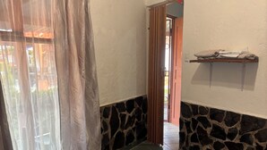 Una habitación con una cama, un muro de piedra, una puerta de madera y un estante con toallas.