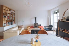 A living room with a fireplace, a sofa, a dining table with a vase, and a bookshelf. - Appartement moderne&charmant, 7e arrondissement ! (Paris)