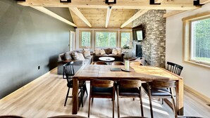 Un salon spacieux avec une grande table à manger en bois, de nombreux espaces pour s’asseoir et une cheminée en pierre.