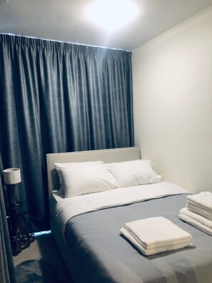 A neatly made bed with white linens, a bedside lamp, and a stack of towels on the right side.