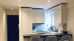 Cuina moderna amb una illa central, tamborets i una porta fosca.
