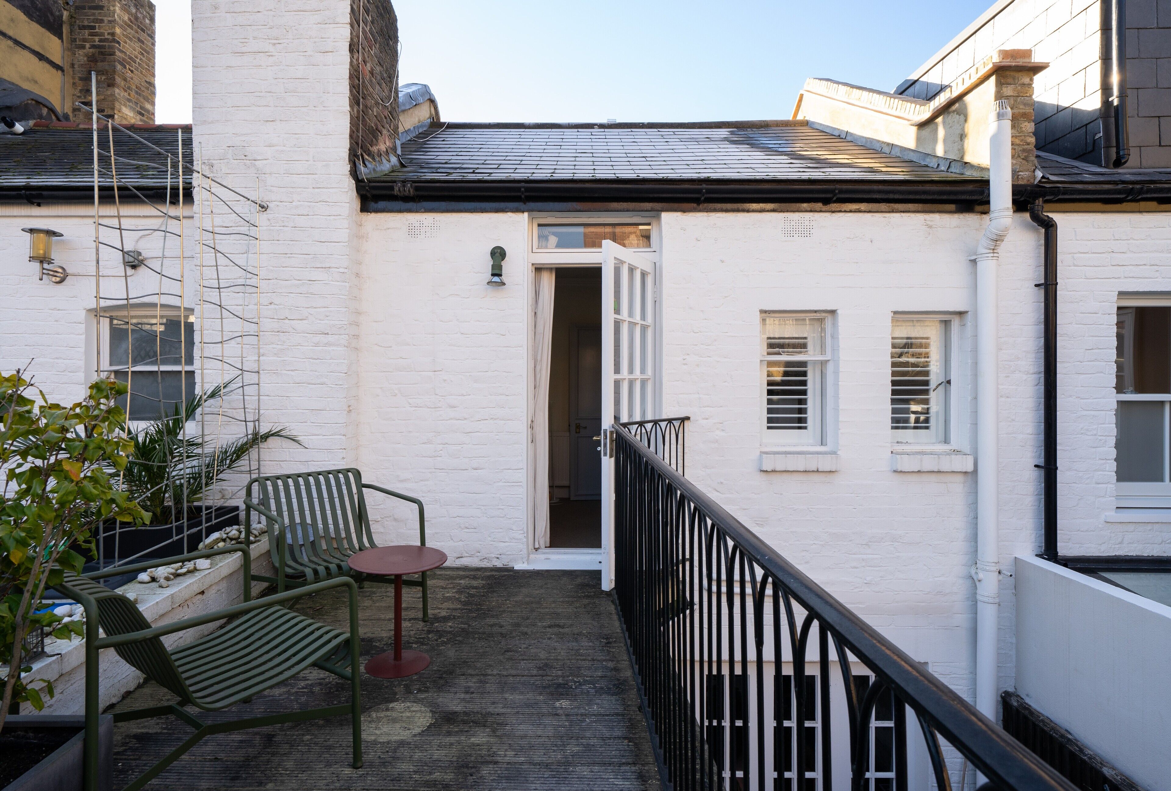 A white building with a black roof, a small outdoor seating area with a table and chairs, and a black railing.