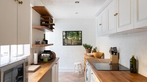 Una cucina compatta con piani in legno, pensili bianchi e un quadro appeso raffigurante un sentiero boschivo.