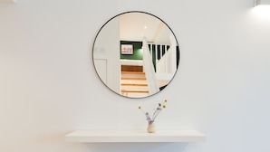 A round mirror on a white wall with a white shelf below it.