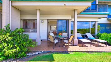 A covered outdoor patio with a dining table and chairs, lounge chairs, and a view of the ocean.