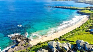 A coastal resort with a beach, clear blue waters, and modern buildings.