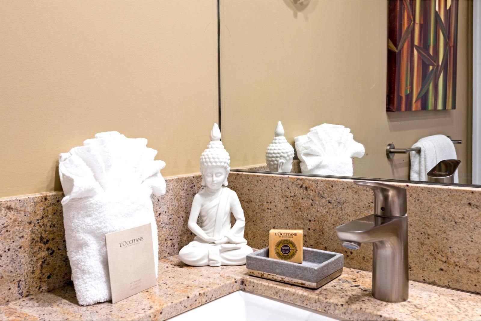 Un baño con encimera de granito, una estatua blanca de Buda, una toalla y un jabonera.
