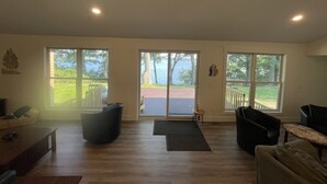 A spacious living room with large windows, a sliding glass door leading to a deck, and a fireplace. - The Perfect Place: Close to town, with 100' of private lake frontage. (Montague)