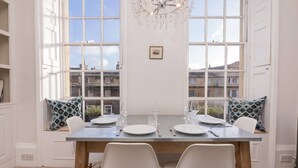 A dining area with a table set for two, large windows, and a chandelier.