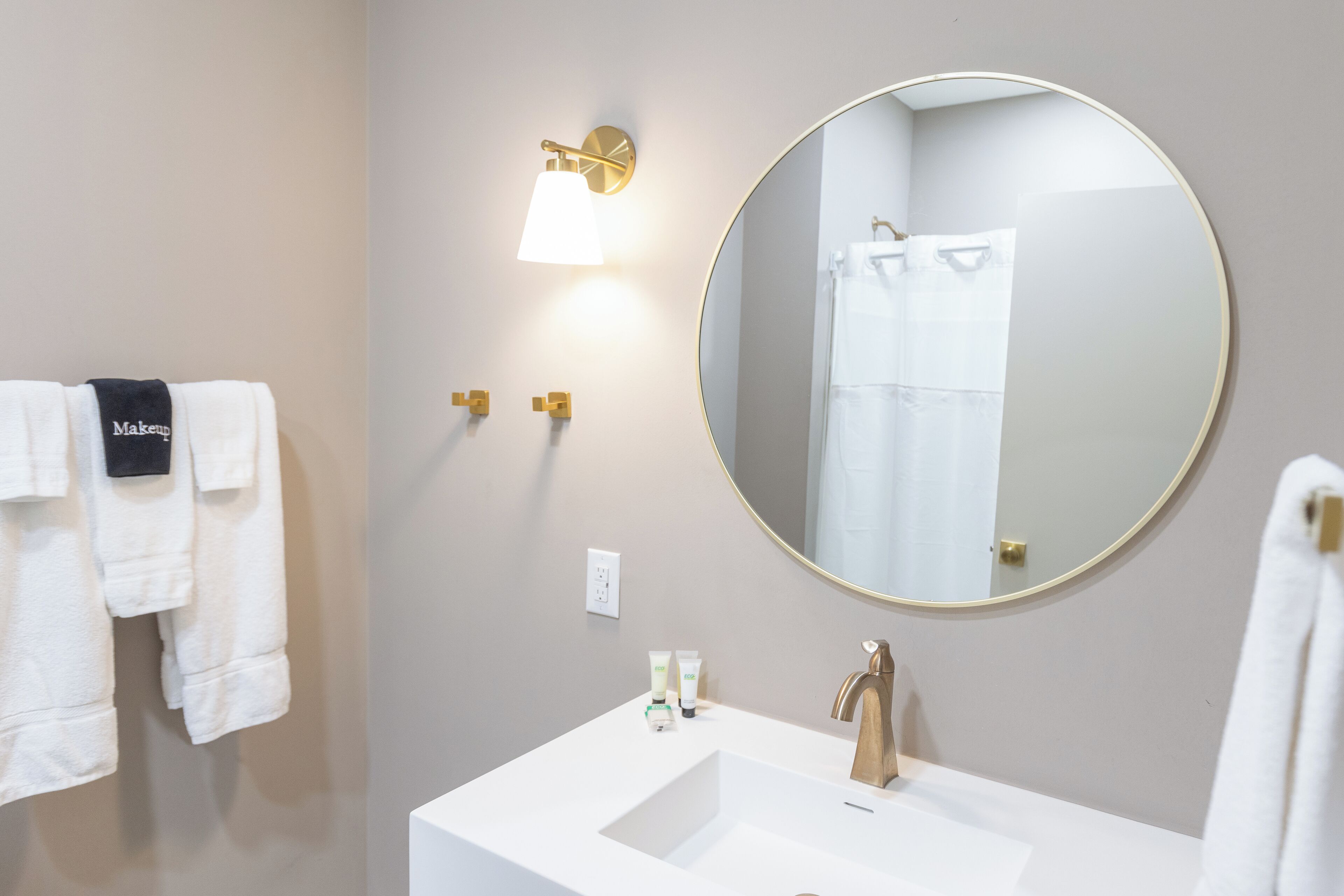 A bathroom with a white sink, a round mirror, and a towel rack with white towels.