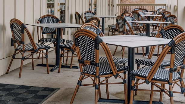 Un patio al aire libre con sillas y mesas de mimbre, un muro de ladrillo y un techo de madera.