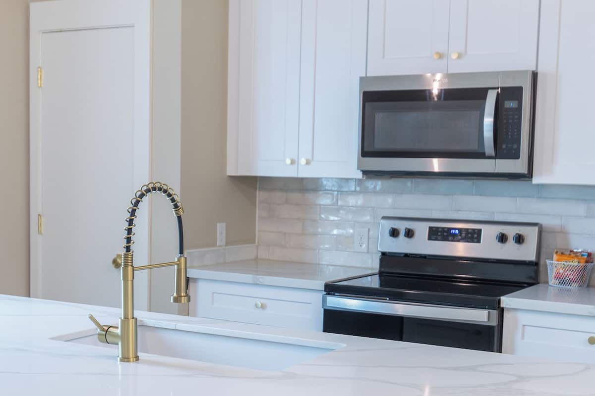 A modern kitchen with white cabinets, a stainless steel microwave, an oven, and a marble countertop.