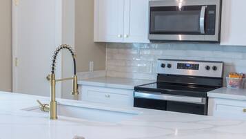 A modern kitchen with white cabinets, a stainless steel microwave, an oven, and a marble countertop.