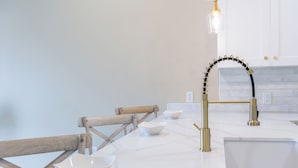 Una cocina con encimera de mármol blanco, grifo dorado y una silla de madera.