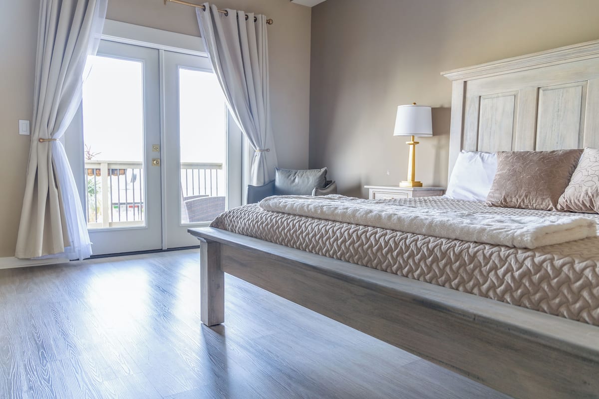 A bedroom with a large bed, a nightstand, a lamp, and a view of the outside.