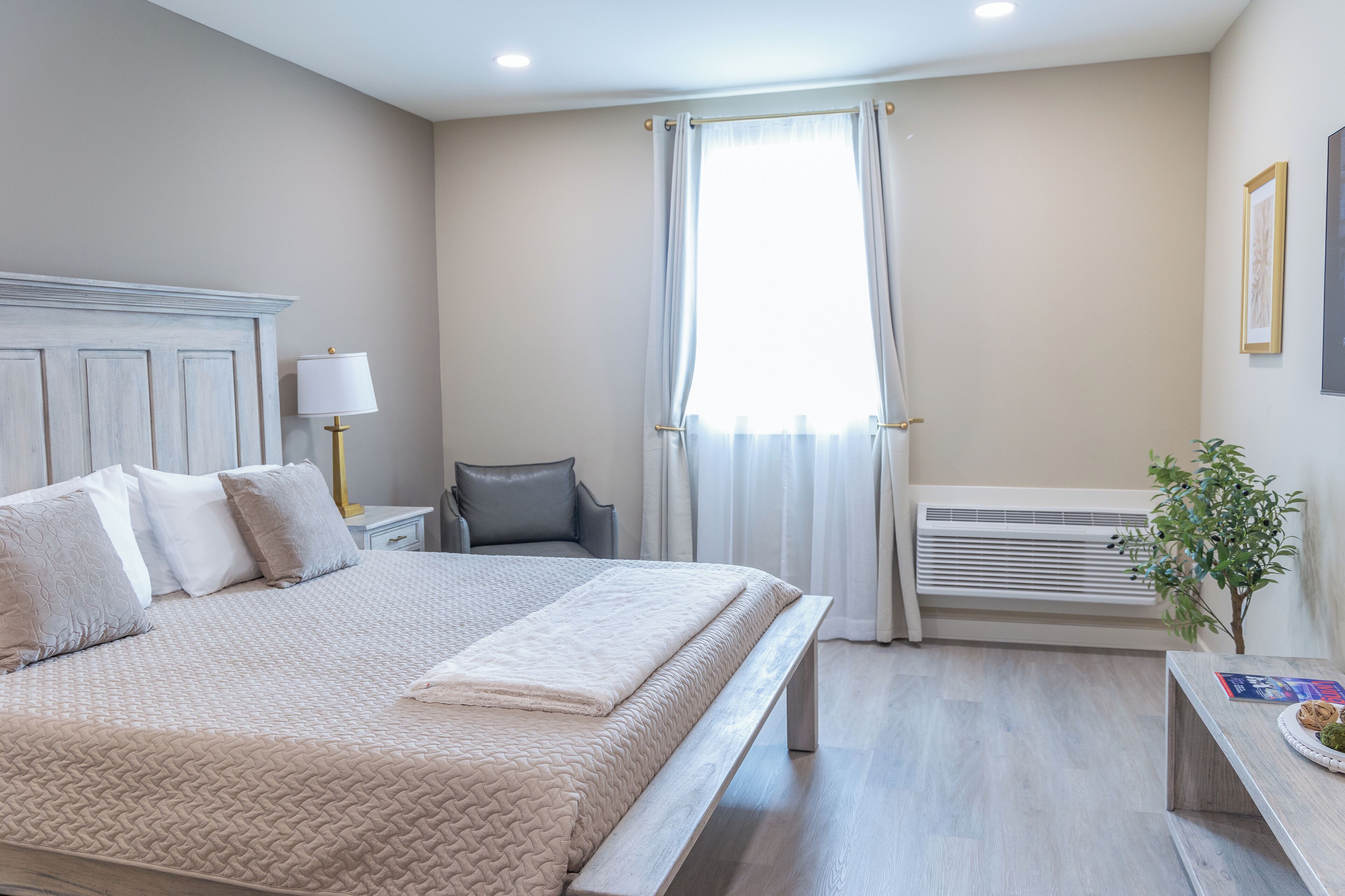 Een slaapkamer met een bed, nachtkastje, lamp, airconditioning en een kleine plant.