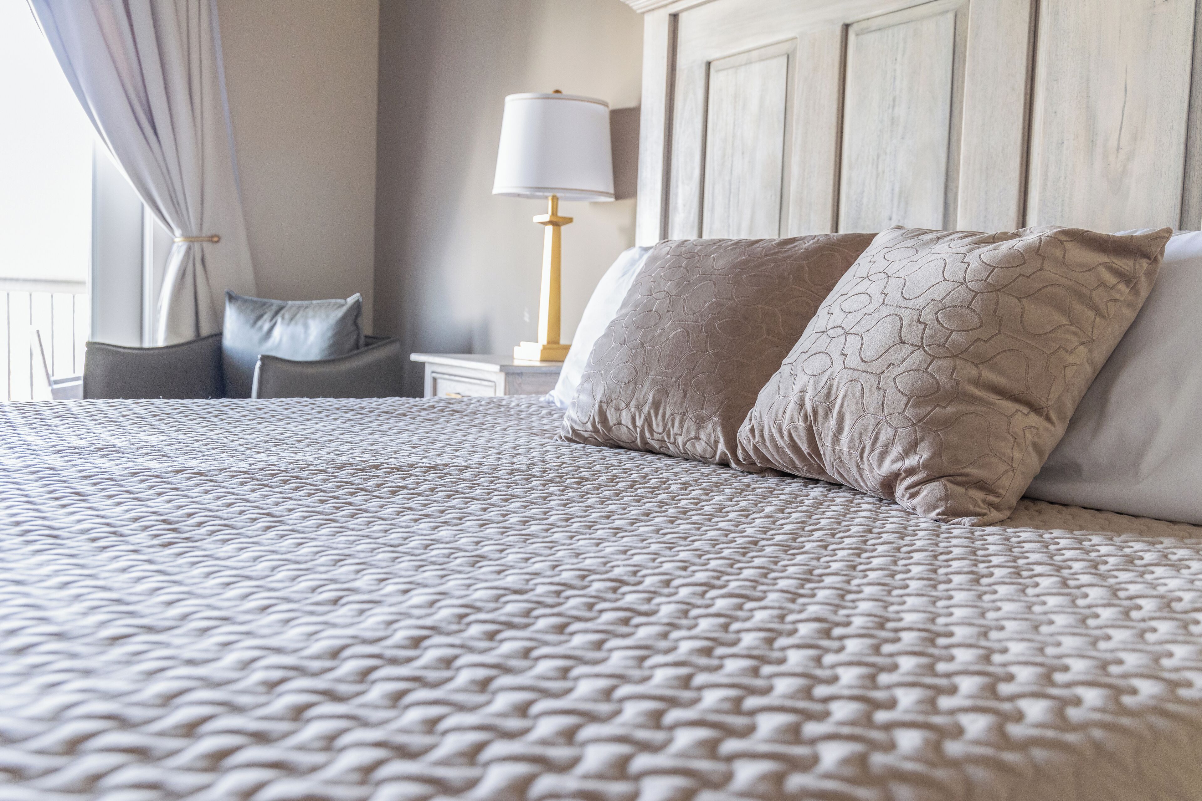 A neatly made bed with a patterned bedspread, a bedside lamp, and a nightstand with a lamp.